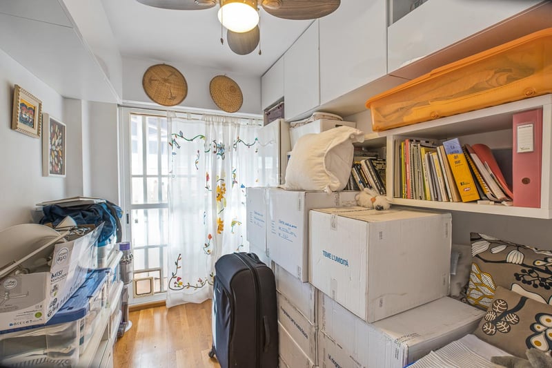 Petite pièce avec placards intégrés blancs, étagères, cartons de déménagement, ventilateur de plafond et fenêtre.