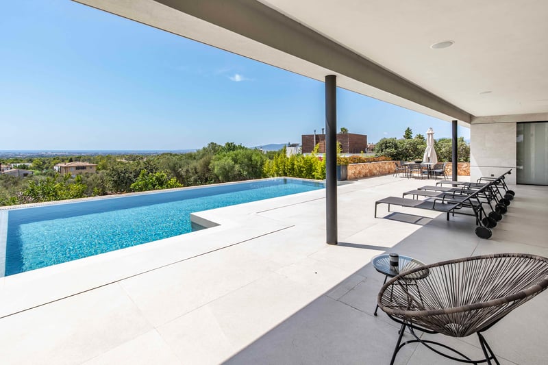 Piscine à débordement sur une terrasse en dalles claires avec chaises longues noires et vue sur la vallée et la mer.