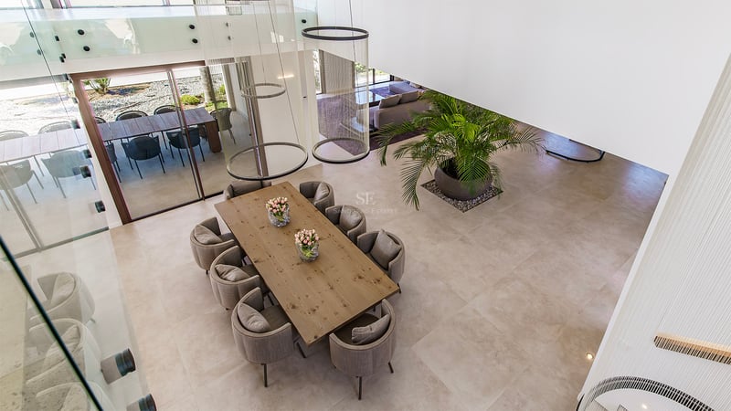 Vue plongeante d'une salle à manger avec table en bois, chaises grises et luminaires suspendus modernes.