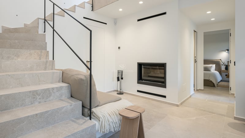 Intérieur moderne avec escalier en pierre claire, rampe noire minimaliste et cheminée murale intégrée.