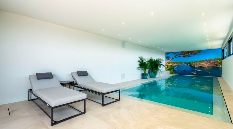 Piscine intérieure moderne avec eau turquoise, chaises longues grises et une grande murale côtière.