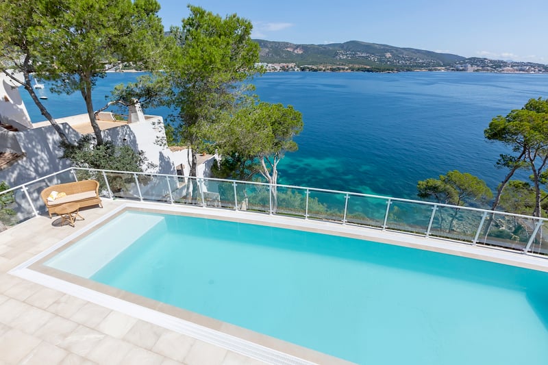 Piscine de luxe avec garde-corps en verre surplombant la mer Méditerranée et le littoral par temps clair.