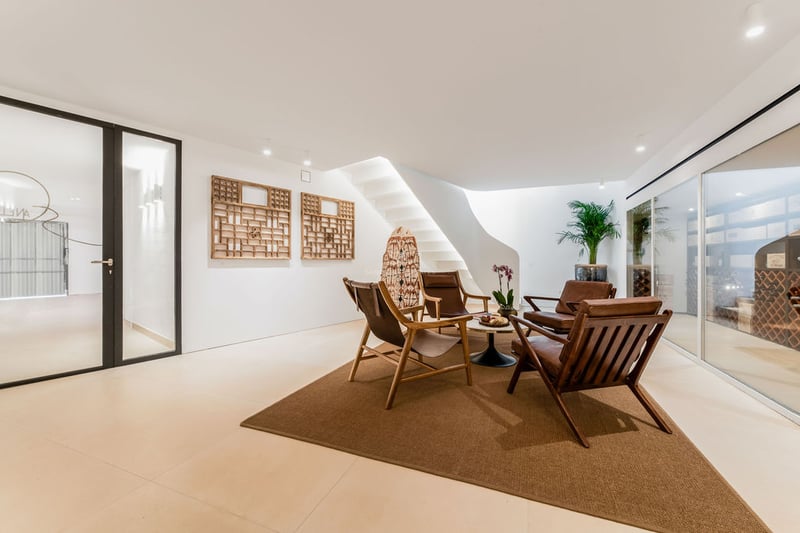 Espace salon moderne avec chaises en cuir, escalier blanc courbé et cave à vin vitrée en arrière-plan.