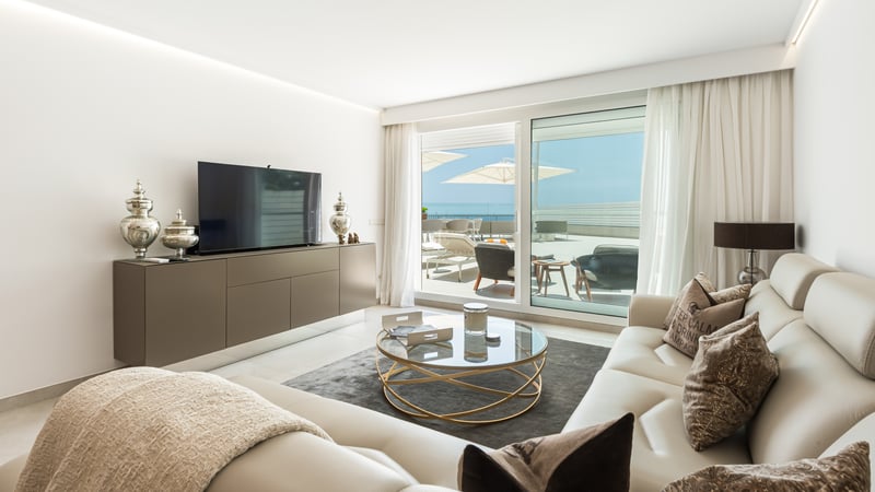 Salon moderne avec canapés en cuir crème, table basse ronde en verre et baies vitrées ouvrant sur une terrasse.