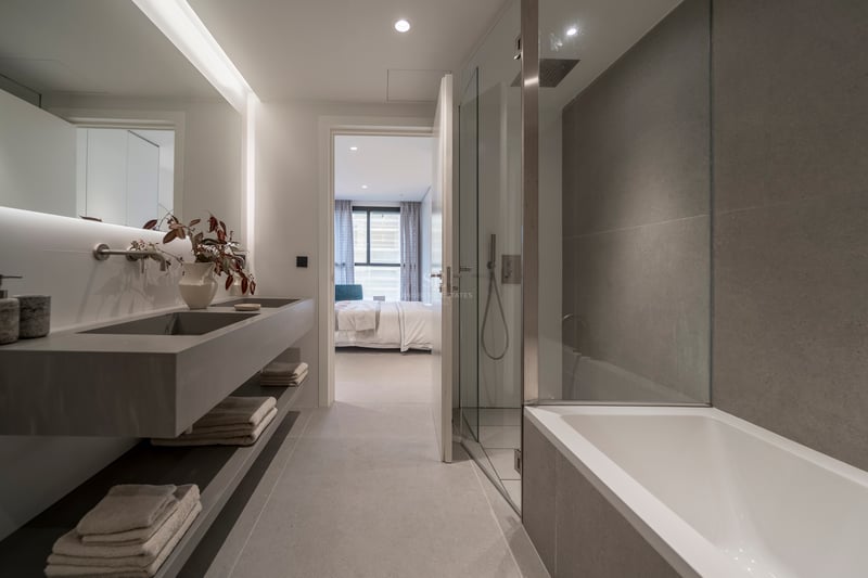 Salle de bain contemporaine avec double vasque grise, douche vitrée, baignoire et vue sur la chambre.