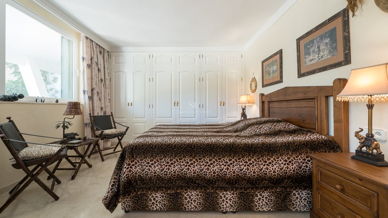 Chambre avec un lit imprimé léopard, des meubles en bois sombre et un mur de placards blancs intégrés.
