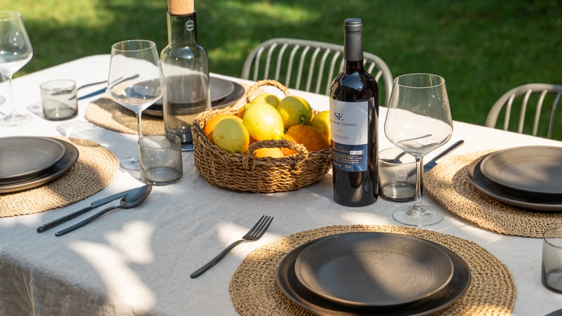 Table de salle à manger extérieure dressée avec du lin, de la vaisselle noire, du vin de Majorque et des citrons.