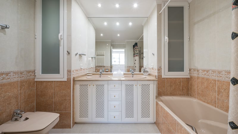 Grande salle de bain avec deux lavabos, grand miroir, baignoire et bidet dans les tons beige et terre cuite.