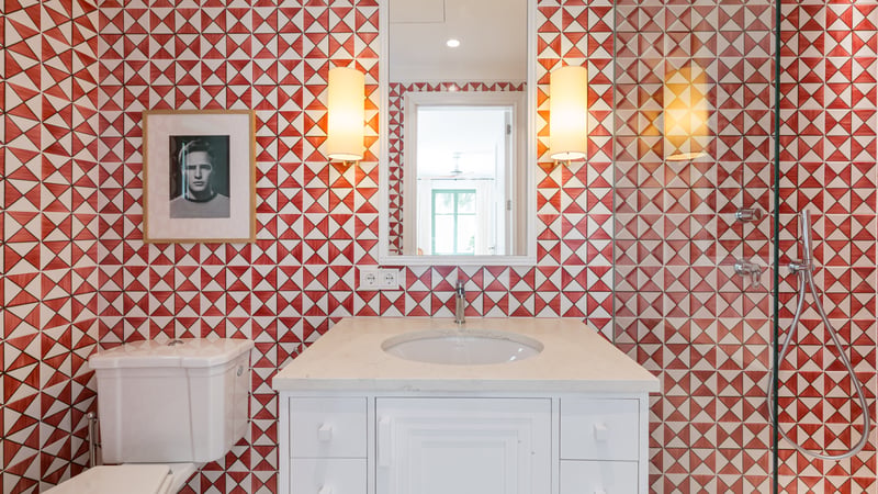 Meuble vasque blanc devant un mur à motifs géométriques rouges et blancs, avec miroir et appliques.