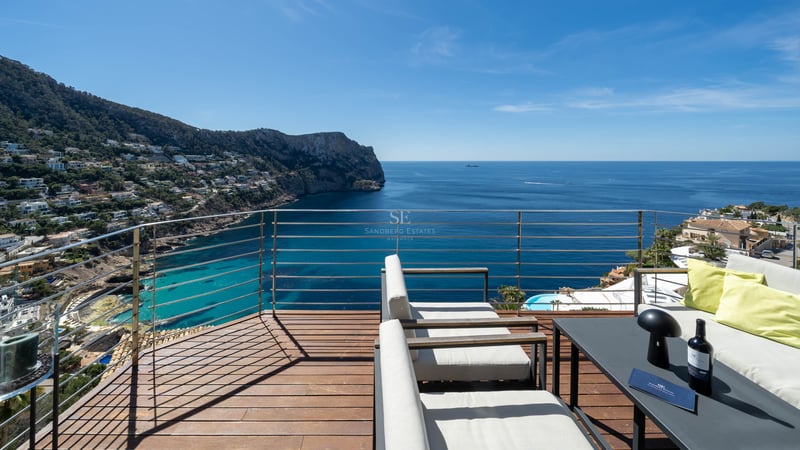 Terrasse en bois surélevée avec salon d'extérieur surplombant une baie méditerranéenne.