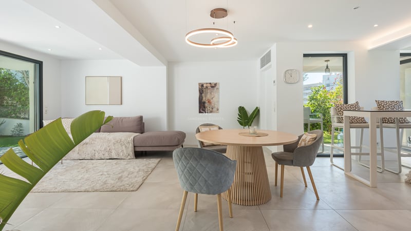 Séjour moderne avec table à manger ronde en chêne, chaises grises et vue sur une terrasse verdoyante.