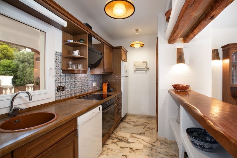 Cuisine étroite avec meubles en bois sombre, sol en marbre, poutres apparentes et crédence en carreaux de ciment.