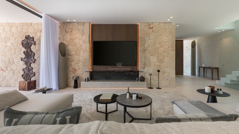 Salon moderne avec mur en pierre naturelle, meuble TV intégré et mobilier minimaliste aux tons neutres.