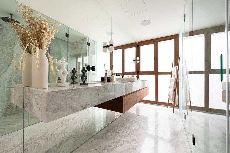 Baño de lujo con lavabo doble de mármol flotante, detalles en madera de nogal y grandes ventanales con marcos de madera.