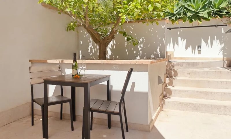 Petite table de bistrot en bois et deux chaises sur un patio en pierre ensoleillé à côté d'un citronnier.
