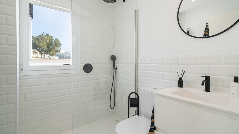 Salle de bain lumineuse avec carrelage métro blanc, paroi de douche en verre et robinetterie noire mate.