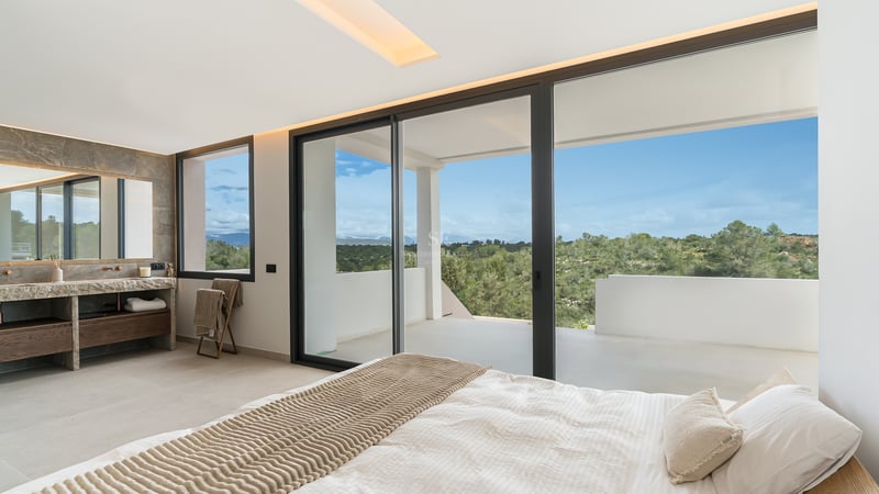 Chambre principale avec grandes baies vitrées coulissantes ouvrant sur une terrasse privée avec vue sur les collines.