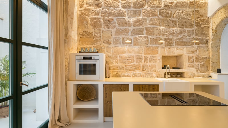 Cuisine moderne avec un grand mur en pierre apparente, des armoires blanches, des accents en bois et des appareils intégrés.