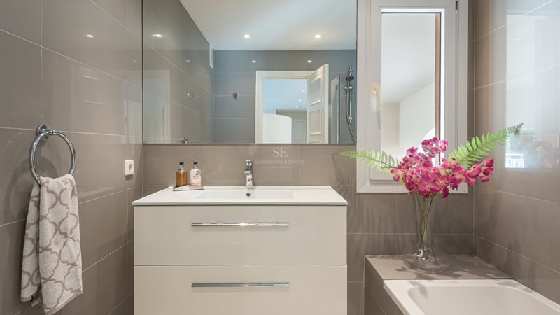 Salle de bains contemporaine avec meuble vasque blanc, grand miroir et carrelage taupe avec accents chromés.