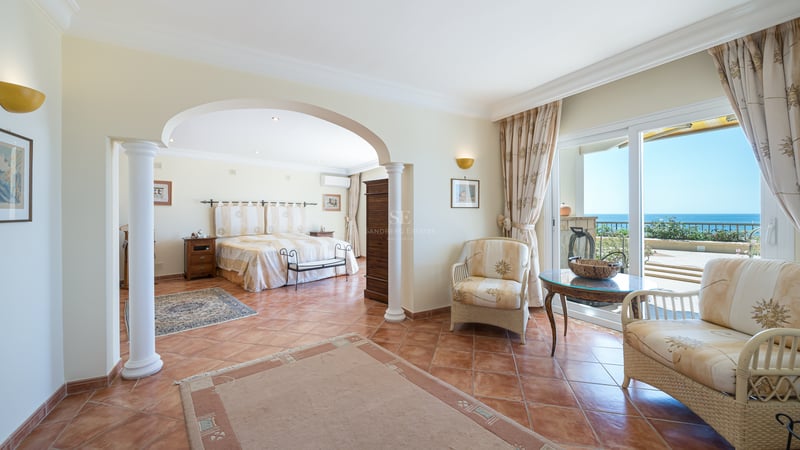 Chambre de style méditerranéen avec sol en terre cuite, colonnes classiques et portes vitrées ouvrant sur la mer.