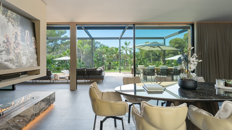 Salle à manger moderne avec table en marbre et cheminée, ouvrant sur une terrasse et un jardin luxuriant.