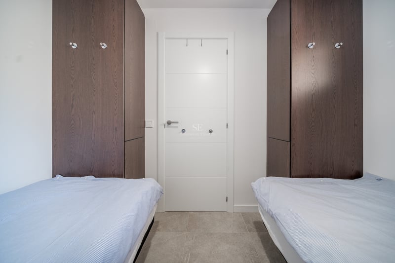 Chambre contemporaine avec lits jumeaux, placards en bois sombre et sol en carrelage gris.