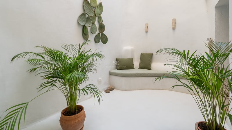 Salon minimaliste blanc avec banquette intégrée incurvée, coussins vert sauge et plantes d'intérieur.