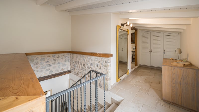 Palier intérieur avec escalier en fer, murs en pierre apparente, poutres en bois et placards intégrés blancs.