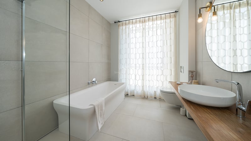 Grande salle de bain avec baignoire blanche, vasque sur plan en bois et paroi de douche en verre.