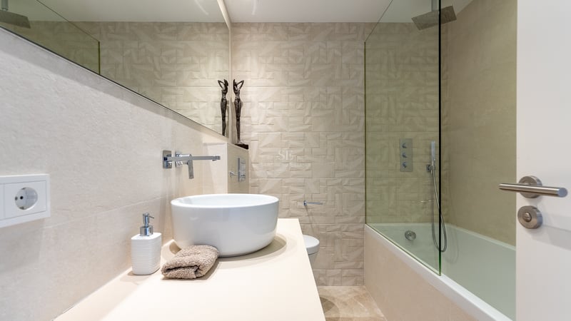 Baño moderno con lavabo sobre encimera, espejo amplio y pared de azulejos geométricos en la zona de ducha.