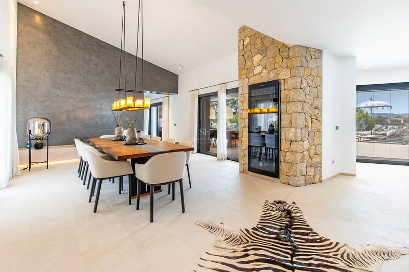 Vue extérieure d'une villa moderne avec piscine à débordement, grandes fenêtres et design minimaliste. Pelouse soignée et ciel dégagé.