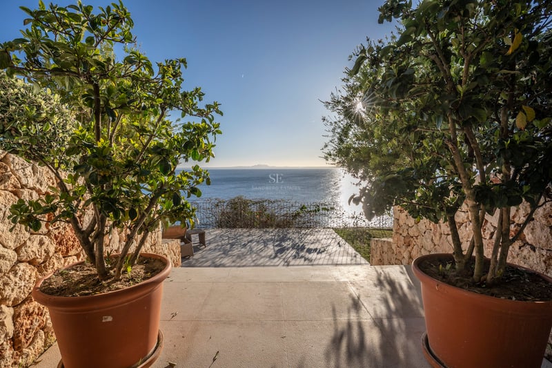Vue sur la mer bleue depuis une terrasse en pierre avec des plantes en pots et des murs en pierre sèche.