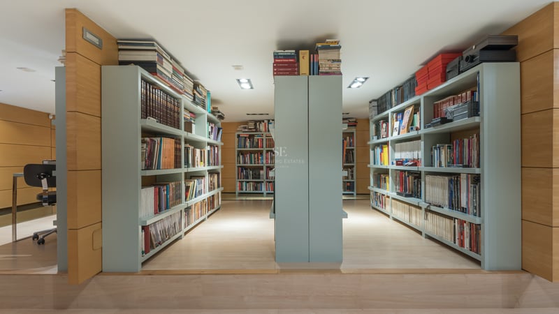 Modern home library with light oak wood paneling and extensive built-in sage green bookshelves.