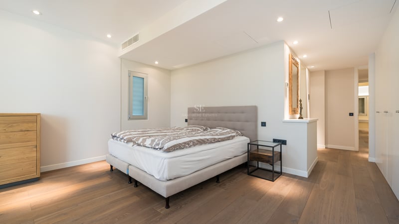 Chambre contemporaine avec lit double, tête de lit taupe, parquet en chêne et éclairage encastré chaleureux.