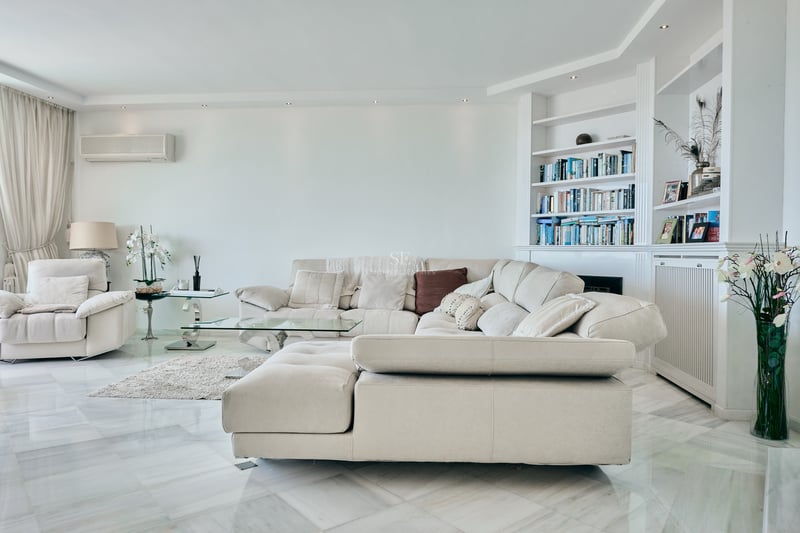 Grand salon avec canapé d'angle beige, sol en marbre poli et bibliothèque intégrée blanche.