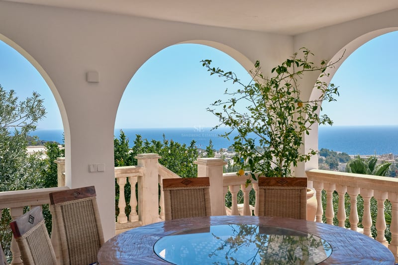 Terrasse couverte avec arches blanches, table ronde et balustrade en pierre surplombant la mer Méditerranée.