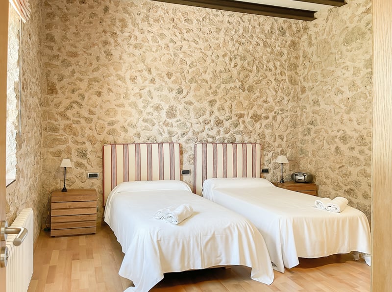 Chambre à deux lits avec murs en pierre apparente, parquet en bois clair et têtes de lit rayées.