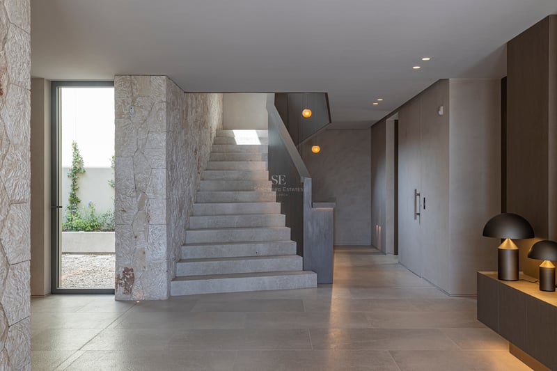Couloir moderne avec escalier en pierre, murs en pierre texturée et éclairage design chaleureux.