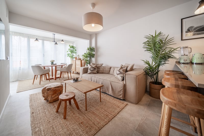 Salon moderne avec canapé beige, tapis en jute, table basse en bois et plantes d'intérieur.