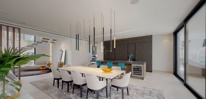 Salle à manger spacieuse avec une longue table blanche, des suspensions design et un îlot de cuisine avec tabourets turquoise.