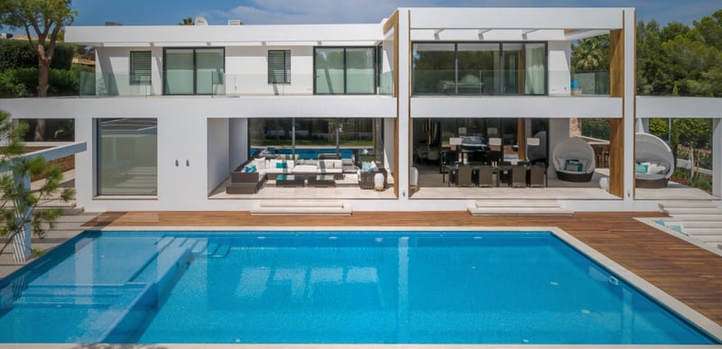 Vue arrière d'une villa contemporaine blanche sur deux niveaux avec piscine turquoise et salon d'été.