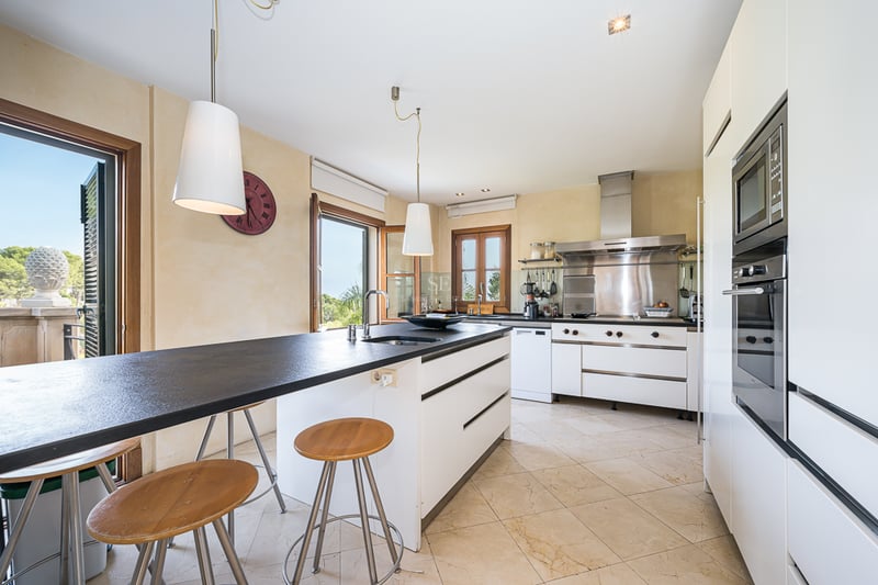 Cuisine moderne avec îlot central noir, tabourets en bois, plan de travail sombre et appareils en acier inoxydable.