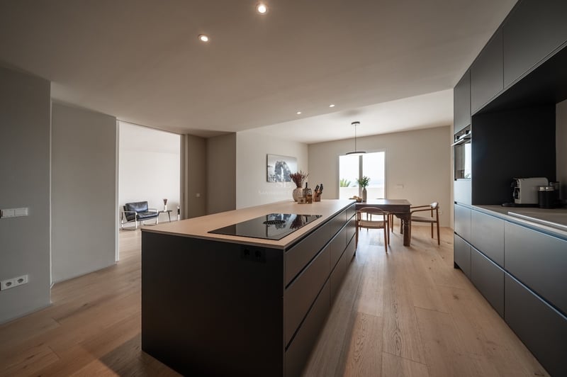 Cuisine moderne avec îlot anthracite, plan de travail en chêne, parquet et coin repas en arrière-plan.