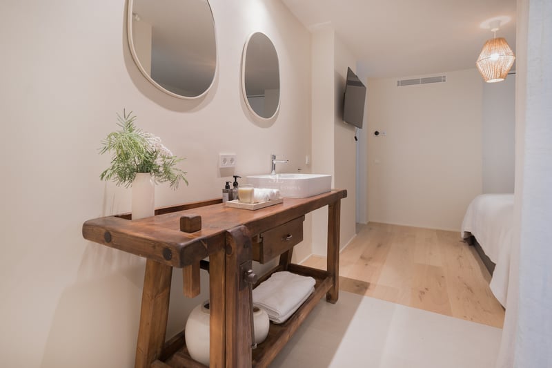 Salle de bain avec meuble en bois massif, vasque blanche et deux miroirs ovales sur mur blanc cassé.