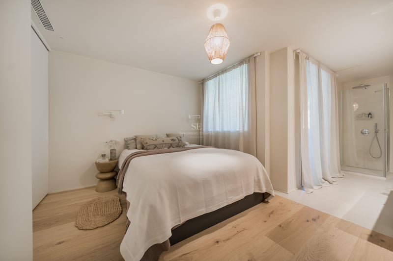Chambre lumineuse avec parquet en chêne clair, literie crème et une suspension design en papier.
