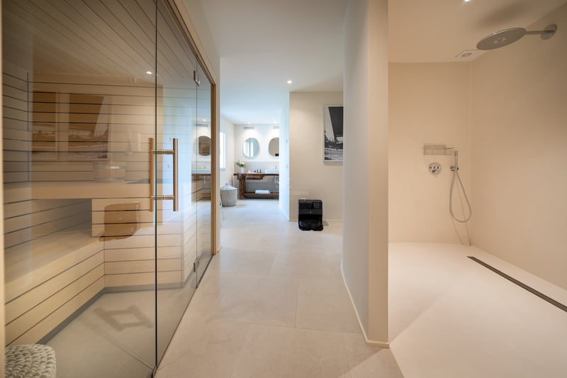 Espace spa intérieur comprenant un sauna vitré, une douche à l'italienne et des sols en pierre claire.
