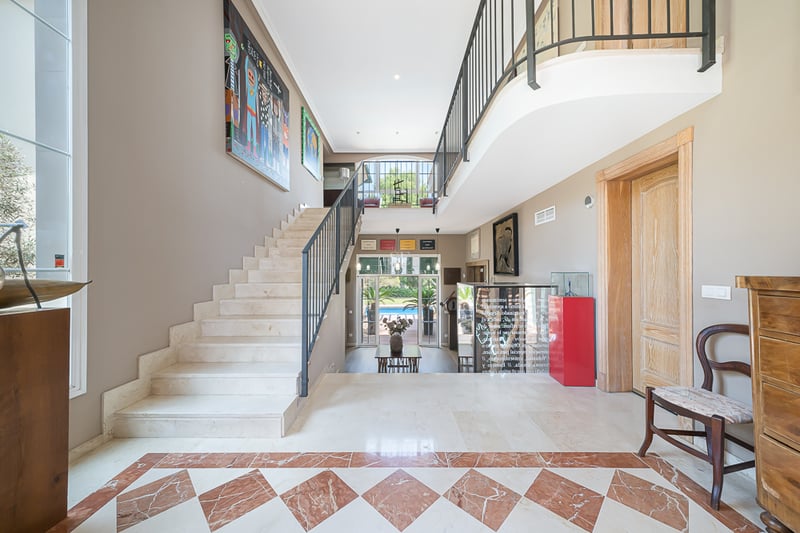 Entrée de villa de luxe avec sol en marbre crème, incrustations en terre cuite et escalier élégant sous plafond haut.