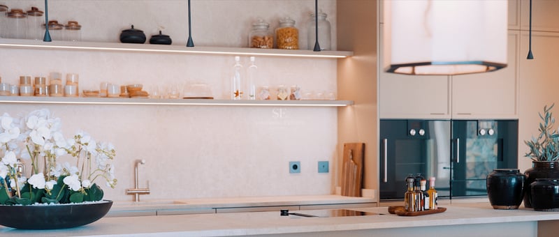 Gros plan d'une cuisine de luxe avec plans de travail en pierre crème, étagères ouvertes éclairées par LED et appareils intégrés.