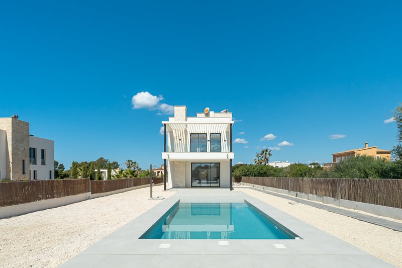 Piscine rectangulaire bleue menant à une villa moderne blanche de deux étages sous un ciel bleu pur.