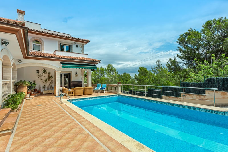 Grande piscine rectangulaire avec mosaïque bleue à côté d'une terrasse en terre cuite et d'une villa classique.